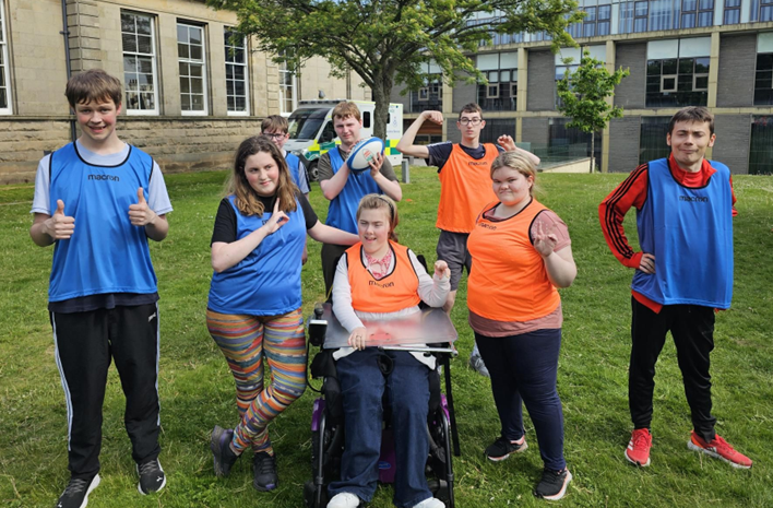 A group photo of our Supported Learning students after participating in a game of Tartan Touch Rugby. They are outdoors on campus, smiling at the camera and wearing sport vests.