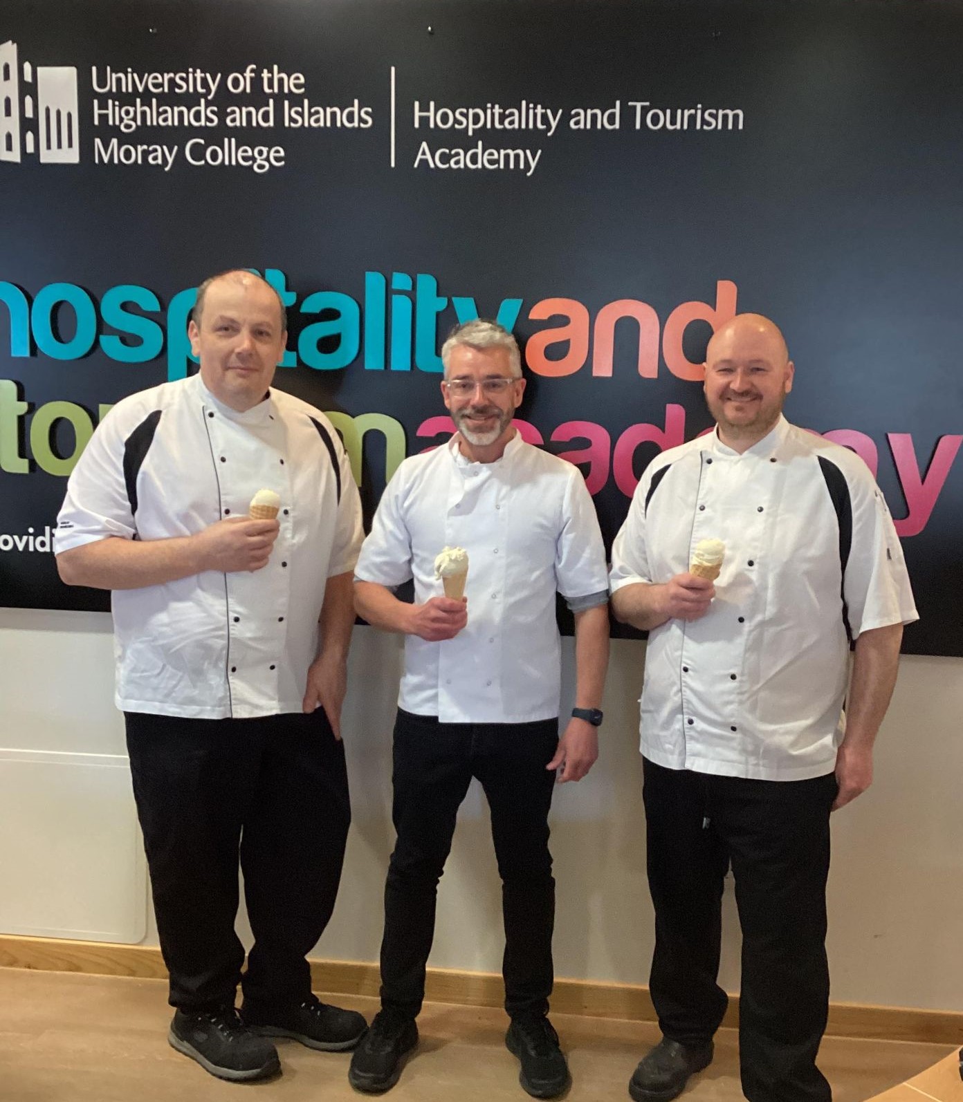 Photograph of two UHI Moray hospitality lecturers, Martyn and Darren, with Stew 'n' Drews staff member. They are all wearing Chef whites and holding an ice-cream each, smiling at the camera.