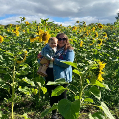 Photograph of Leigh Miele, Training Co-Ordinator for Employability at UHI Moray, standing in a sunflower field and holding her daughter